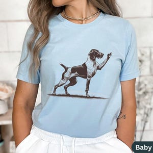 May include: A light blue t-shirt with a graphic of a German Shorthaired Pointer dog giving the middle finger. The text "Baby Blue" is visible in the bottom right corner of the image.