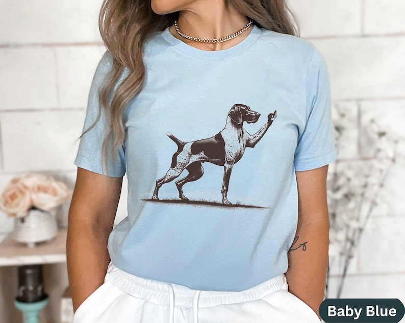 May include: A light blue t-shirt with a graphic of a German Shorthaired Pointer dog giving the middle finger. The text "Baby Blue" is visible in the bottom right corner of the image.