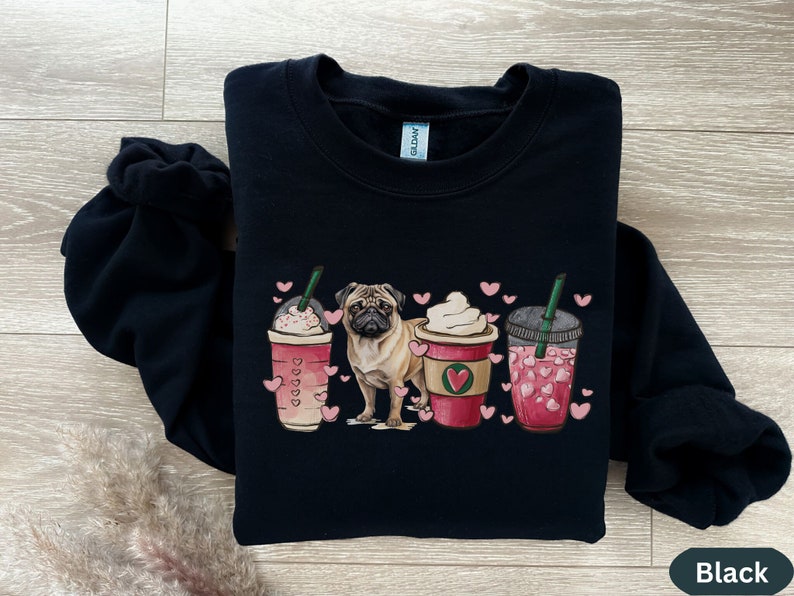 May include: Black sweatshirt with a pug dog and three pink and white coffee cups with hearts. The cups have green straws and are surrounded by pink hearts.