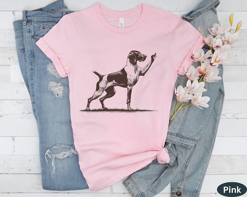 May include: A pink t-shirt with a black and white illustration of a German Shorthaired Pointer dog giving the middle finger.