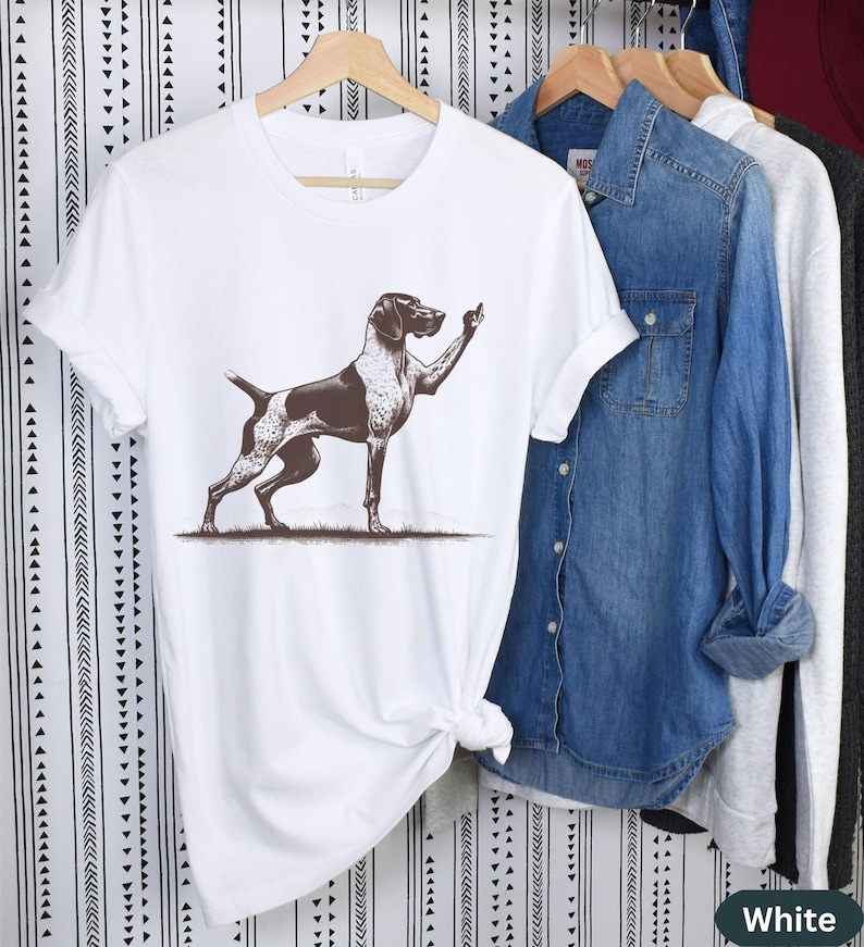 May include: White t-shirt with a brown and white German Shorthaired Pointer dog illustration. The dog is standing on its hind legs with its front paw raised in a gesture of giving the middle finger.
