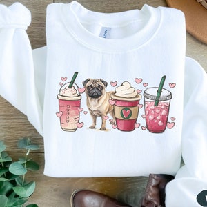 May include: White sweatshirt with a pug dog and three coffee cups with hearts on them. The cups are filled with pink and white beverages. The text "White" is in the bottom right corner of the image.