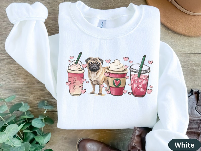 May include: White sweatshirt with a pug dog and three coffee cups with hearts on them. The cups are filled with pink and white beverages. The text "White" is in the bottom right corner of the image.