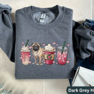 May include: Dark grey heather sweatshirt with a graphic of a pug dog and three coffee drinks with hearts. The coffee drinks are a caramel macchiato, a vanilla latte, and a strawberry refresher.