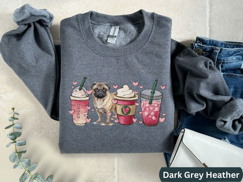 May include: Dark grey heather sweatshirt with a graphic of a pug dog and three coffee drinks with hearts. The coffee drinks are a caramel macchiato, a vanilla latte, and a strawberry refresher.