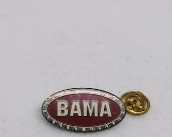 Könnte beinhalten: Ein ovaler Pin in Rot und Weiß mit dem Wort "BAMA" in weißen Buchstaben. Der Pin hat die Worte "Roll Tide" wiederholt um den Rand herum.