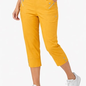 May include: Mustard yellow capri pants with silver zipper pockets and button details. The cropped pants have a comfortable elastic waistband and are paired with white sneakers. A casual, everyday style.