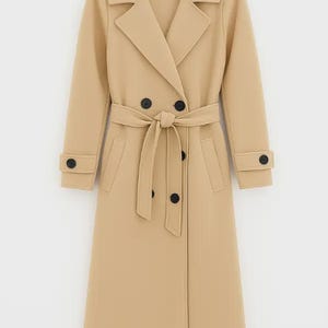 Könnte beinhalten: Ein beigefarbener Trenchcoat mit doppelreihigem Design, schwarzen Knöpfen und passendem Gürtel. Der Mantel hat einen klassischen Reverskragen, lange Ärmel und Taschen. Ein stilvolles Oberbekleidungsstück.