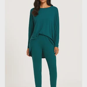 May include: A teal loungewear set. The ensemble features a long-sleeved top with a round neck and matching trousers. The material looks soft and comfortable, ideal for relaxing or casual wear. The outfit is a solid colour.