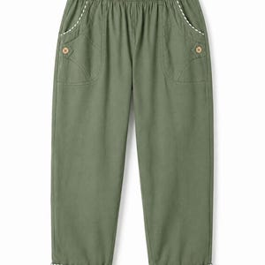 May include: Olive green trousers featuring an elasticated waistband, two front pockets with decorative light-coloured buttons, and white and olive green vertical striped trim along the pocket edges and the folded cuffs at the bottom of the legs.