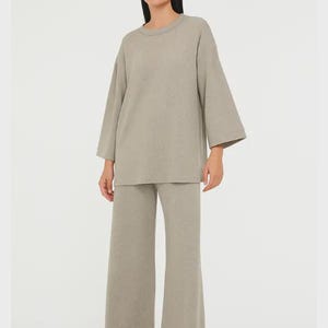 Puede incluir: Conjunto de dos piezas de ropa casual en color beige neutro. El conjunto incluye una parte superior de manga larga y holgada y pantalones de pernera ancha. La modelo lleva el conjunto con sandalias beige. El conjunto está hecho de una tela suave y texturizada.