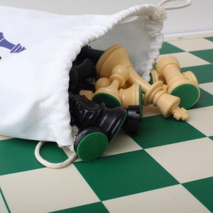 May include: A white canvas bag with the text "Crown Chess" printed on it, spilling out a set of black and cream chess pieces onto a green and cream checkered chessboard.