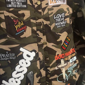 May include: Camouflage print jacket with multiple patches. Patches include the words "Blessed", "Love Them Anyway", "Prayer changes things", and "I'm not perfect but I'm a limited edition". Other patches feature a high heel and a cross.