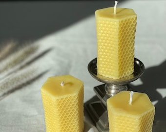 May include: Three yellow honeycomb candles with white wicks. The candles are on a white linen tablecloth.