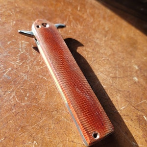 May include: A red pocket knife with a textured handle and a silver blade. The knife is closed and has a small hole in the handle.