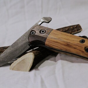 May include: A folding knife with a wooden handle and a partially open blade. The handle is made of two different types of wood, one dark and one light. The blade is made of metal and has a slight curve to it.