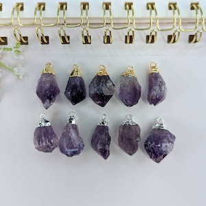 May include: Ten amethyst crystal pendants with gold and silver accents. The pendants are arranged in two rows on a white surface.