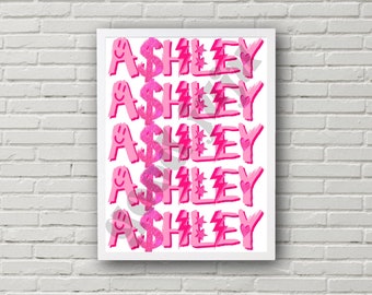 May include: A white framed print with the name "Ashley" repeated five times in pink with glitter, dollar signs, stars, and lightning bolts.
