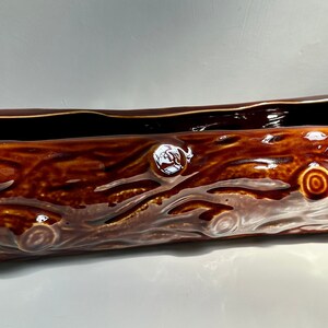 May include: A brown ceramic planter shaped like a log with a textured surface. The planter has a rectangular opening for planting.