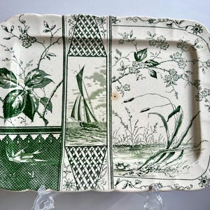 May include: A white ceramic serving tray with a green floral design. The tray features a sailboat, a bird, and a floral pattern.