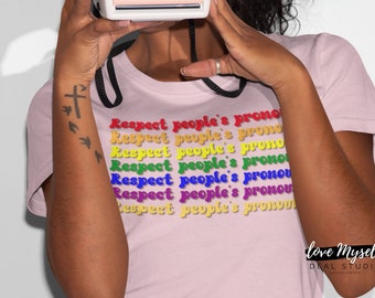 May include: A pink t-shirt with the text "Respect people's pronouns" repeated in rainbow colors. The text is in a retro font style. The shirt has a crew neck and short sleeves. The text "love Myself" and "DEAL STUDIO" are visible at the bottom of the shirt.