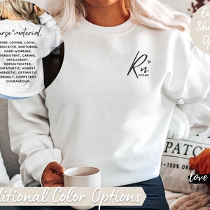 May include: White sweatshirt with the text "nurse material" and a list of positive attributes. The sweatshirt also has a black design with the text "Rn" and the name "Suzan" on the front.