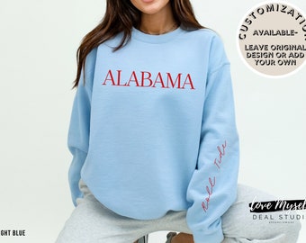 May include: Light blue sweatshirt with the word "ALABAMA" in red on the front and "Roll Tide" in red on the sleeve.