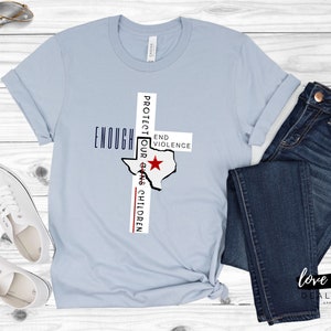 May include: Light blue t-shirt with a white outline of the state of Texas and the text "Protect Our Children" and "Enough End Violence" on either side of the state outline.