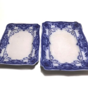 Puede incluir: Dos platos cuadrados antiguos con centro blanco y borde floral azul. Los platos tienen una forma asimétrica única y probablemente son de porcelana o cerámica. El diseño azul incluye motivos florales y de volutas.