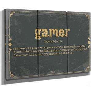 May include: A three-panel wall art piece with a dark gray background and gold text and accents. The word "gamer" is displayed in large gold letters, with a definition below. The definition describes a person who plays video games.