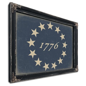 May include: Framed wall art featuring a distressed blue background with a circle of beige stars and the year "1776" in the center. The artwork is encased in a black ornate frame, adding a vintage aesthetic. The piece is designed to be hung on a wall.