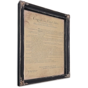May include: A framed document with the text "Congrefs of the United States" in a black distressed frame. The document is aged with a parchment-like appearance. Ornate corner details add a decorative touch to the frame.