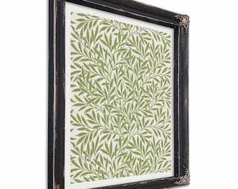 May include: A framed print featuring a green and white botanical pattern of leaves and branches. The print is set within a black, distressed-look frame with decorative corner accents. The artwork has a vintage aesthetic.