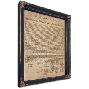 May include: Framed print of the Declaration of Independence. The document is displayed in a black frame with ornate corner details. The text is in a vintage style, with signatures at the bottom. The frame has a distressed finish.