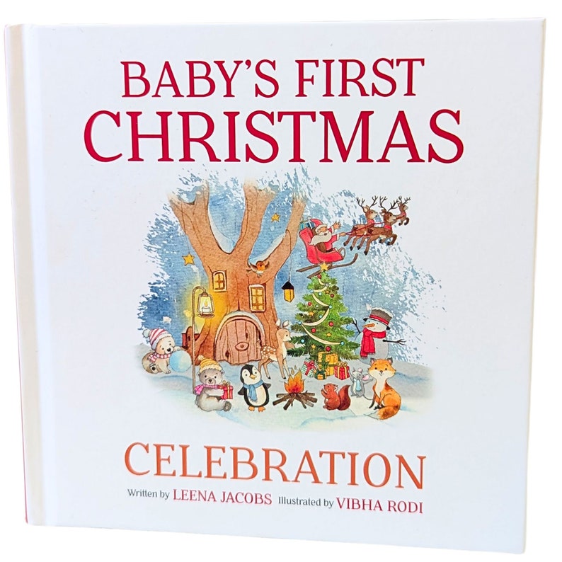 May include: A hardcover book titled "BABY'S FIRST CHRISTMAS CELEBRATION" with a festive illustration. The cover features a winter scene with Santa in a sleigh, a decorated Christmas tree, and woodland creatures. The author is Leena Jacobs, and the illustrator is Vibha Rodi.