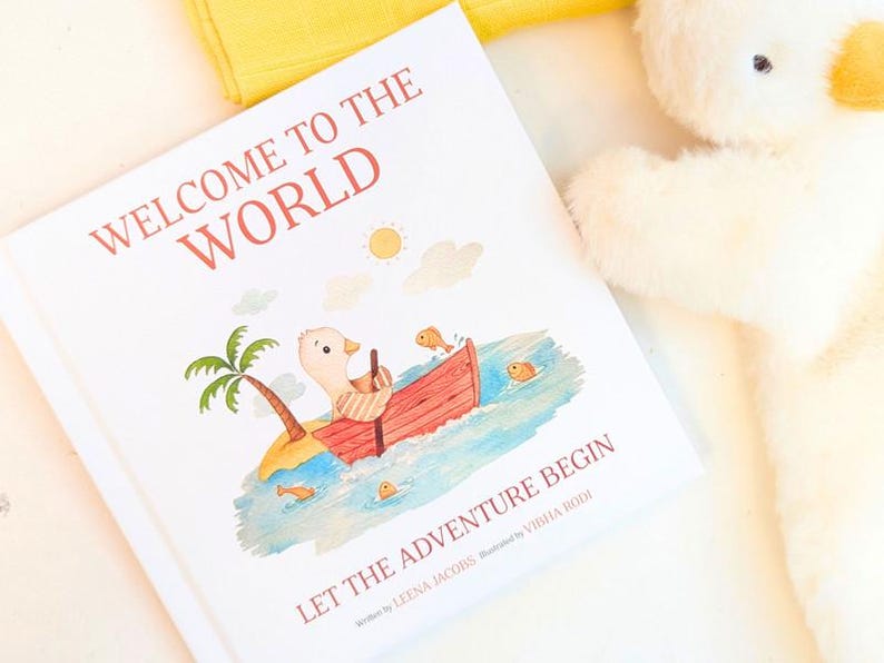May include: A children's book titled "Welcome to the World" with an illustration of a duck in a boat. The book cover features a palm tree, sun, and the text "Let the Adventure Begin". A plush duck toy is in the background.