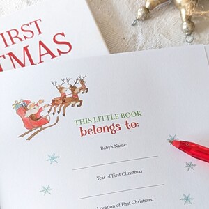 May include: A Christmas-themed baby book with the text "FIRST CHRISTMAS" in red. The inside page features a Santa Claus illustration in a sleigh pulled by reindeer, with space to write the baby's name and the year and location of their first Christmas.