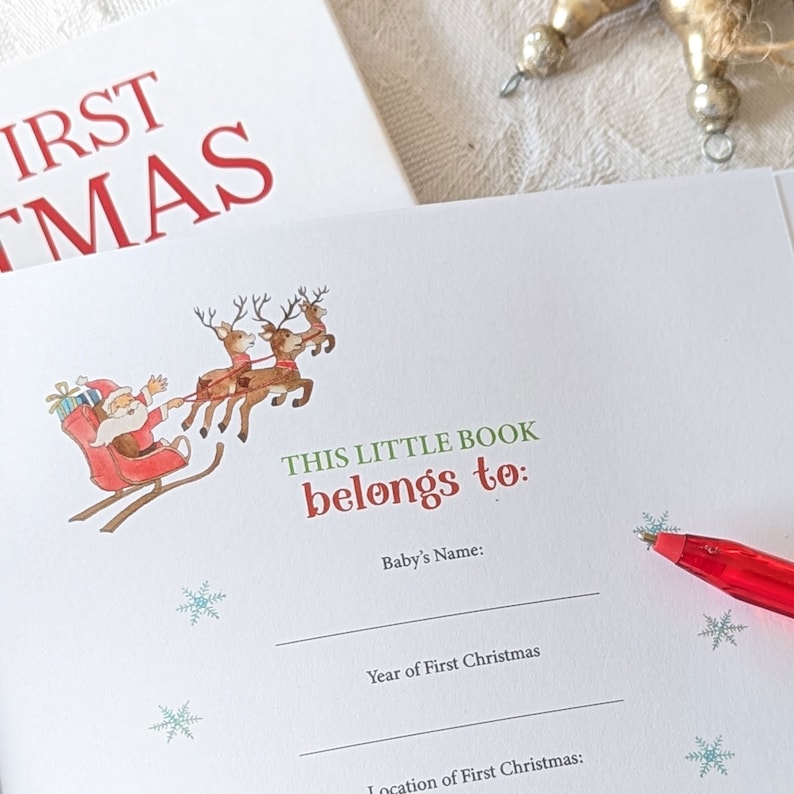 May include: A Christmas-themed baby book with the text "FIRST CHRISTMAS" in red. The inside page features a Santa Claus illustration in a sleigh pulled by reindeer, with space to write the baby's name and the year and location of their first Christmas.