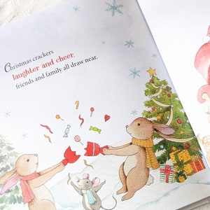 May include: A children's book illustration featuring two brown rabbits and a gray mouse celebrating Christmas. The text reads "Christmas crackers, laughter and cheer, friends and family all draw near." A decorated Christmas tree and gifts are in the background.