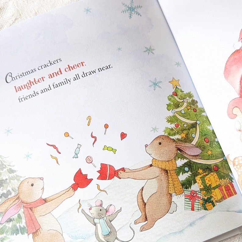 May include: A children's book illustration featuring two brown rabbits and a gray mouse celebrating Christmas. The text reads "Christmas crackers, laughter and cheer, friends and family all draw near." A decorated Christmas tree and gifts are in the background.