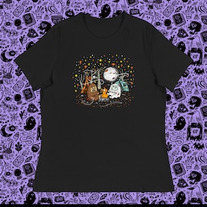 May include: A black t-shirt with a graphic of a campfire scene featuring a yeti, a bear, and a fox. The scene is set in a forest with trees, stars, and a full moon.