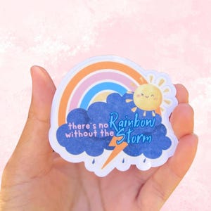 May include: A colorful sticker featuring a rainbow, sun, and clouds. The sticker has the text "there's no rainbow without the storm". The rainbow has orange, pink, and blue stripes. The sun has a smiling face.