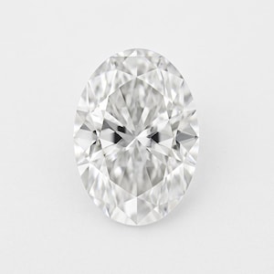May include: A dazzling oval-cut diamond, displaying numerous facets that catch and reflect light. The gemstone is set against a plain white backdrop, highlighting its clarity and brilliance. The shape is elongated, with a symmetrical design.