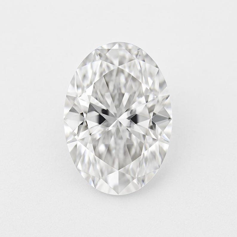 May include: A dazzling oval-cut diamond, displaying numerous facets that catch and reflect light. The gemstone is set against a plain white backdrop, highlighting its clarity and brilliance. The shape is elongated, with a symmetrical design.