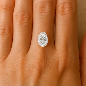 May include: A dazzling oval-cut diamond, displayed against a warm skin tone. The gemstone's facets catch the light, creating a sparkling effect. The diamond's clarity and shape are highlighted. A piece of fine jewellery.