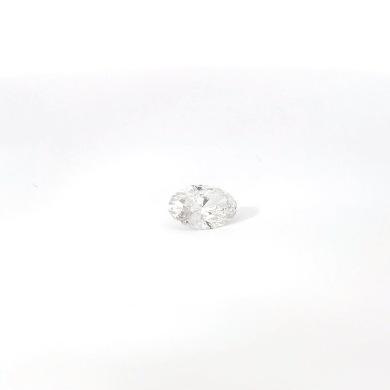 May include: A clear, oval-cut diamond with multiple facets, reflecting light. The gemstone is set against a white background, showcasing its brilliance and clarity. This diamond is a symbol of luxury and elegance.