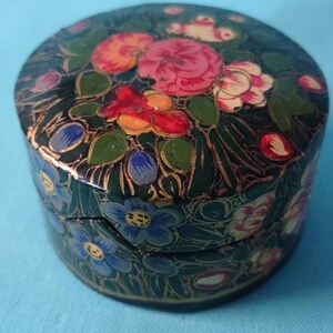 May include: A small, round, black box with a hinged lid. The box is decorated with a floral pattern in shades of pink, red, blue, green, and gold.