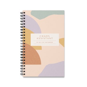 Puede incluir: Una libreta de espiral rosa con un diseño abstracto que presenta formas geométricas en tonos marrones, amarillos, verdes y morados. La libreta tiene el texto "Chaos Assistant To Do List Notebook" impreso en la portada.