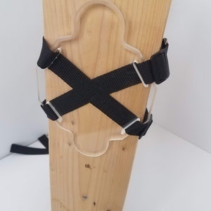May include: A wooden post with a clear plastic cutout and black straps attached to it. The straps are crossed in an X shape.
