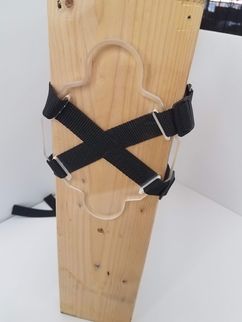 May include: A wooden post with a clear plastic cutout and black straps attached to it. The straps are crossed in an X shape.